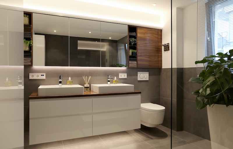 Badezimmer mit teilweise verspiegelter Schrankfront oben und weißem Badezimmerschrank unten mit Holzoberfläche und Porzelan Waschbecken
